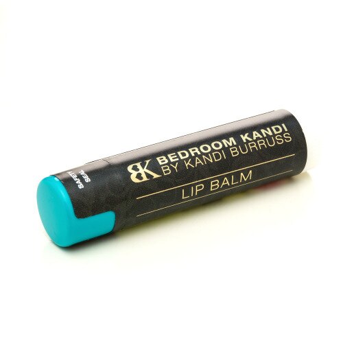 An image of a rube of Bedroom Kandi natural lip butter in Guavalava flavor lying on its side on a white background. It has a black and gold label and a teal cap.